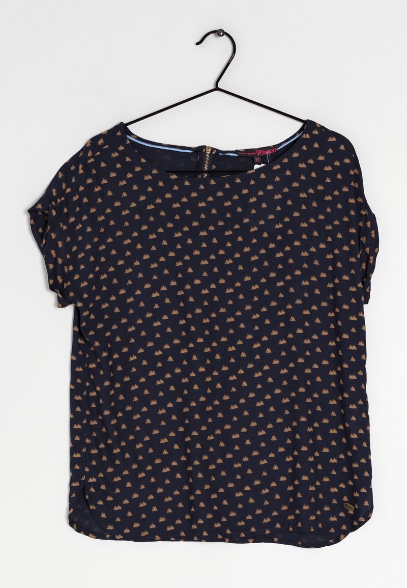 Blouse bleu marine à manches courtes avec un petit motif triangulaire beige, encolure ronde et fermeture éclair au dos, suspendue à un cintre noir.
