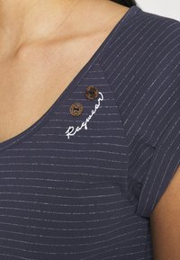 Marinrandig topp med v-ringning, tre dekorativa träknappar och vit broderad text som lyder "Ragwear" på axelsömmen.