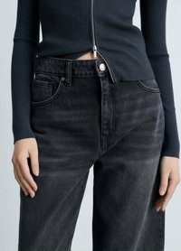 Črne denim hlače z visokim pasom, petimi žepi in rahlimi obrabljenostmi. V kombinaciji z oprijetim mornarsko modrim rebrastim vrhom.