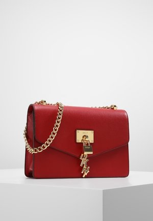 Rode leren handtas met gouden kettingriem, gouden slot en DKNY letterbedels op een wit voetstuk tegen een effen achtergrond.