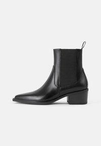 Bottines noires en cuir au design épuré, à bout pointu, avec des panneaux latéraux élastiques et un talon bas carré. Fini texturé avec détail de tirage.