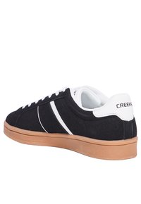 Schwarze Wildleder-Sneaker mit weißen Akzenten und Schnürsenkeln, ausgestattet mit einer hellbraunen Gummisohle. Enthält ein Markenlogo an der Ferse.