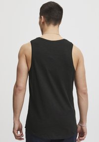 Top negru cu bretele, fabricat dintr-un material moale și ușor. Prezintă un decolteu rotund și găuri largi pentru brațe. Textură netedă, cu o croială lejeră.