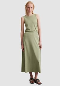 Light green, sleeveless dress in a fitted top and flowing maxi skirt; made of soft fabric with a smooth texture. Black sandals with buckles.