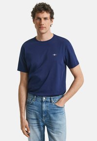 Marineblauwe katoenen T-shirt met een ronde hals en korte mouwen, voorzien van een klein logo op de borst. Draagt met lichtblauwe spijkerbroek.