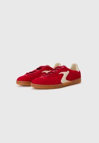 Røde semskede sneakers med en beige accent, gummisål og snørelukning. Har en rund tå og diskrete syninger.