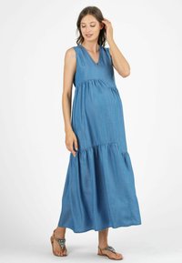 Abito lungo in denim con scollo a V, senza maniche, gonna a strati e vestibilità ampia. Il colore è blu medio con una trama liscia.
