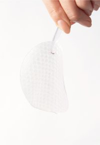 Klebende silikon brystpute, semi-transparent med en teksturert overflate. Den holdes av en klar tab, med en buet, anatomisk form.