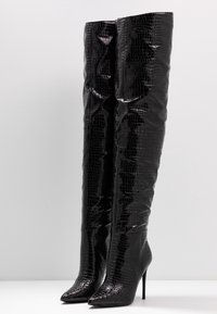 Botas negras hasta la rodilla con una textura de cocodrilo brillante, punta afilada y tacón de aguja. El diseño presenta detalles arrugados en el tubo.