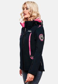 Woman wearing a black and pink softshell jacket with hood and logo patches, standing in profile against a white background.