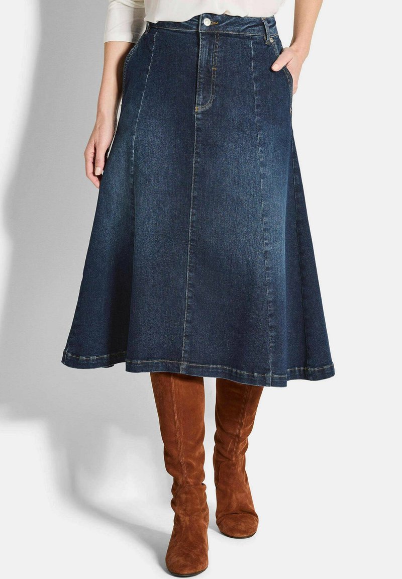 Jupe A-line en jean bleu foncé avec une texture lisse, dotée d'une taille ajustée, de poches avant et d'un ourlet évasé. Portée avec des bottes brunes jusqu'aux genoux.