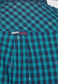 Camicetta a maniche corte con motivo a quadri turchese e blu scuro, con piega e dettagli in tessuto a contrasto sullo scollo.