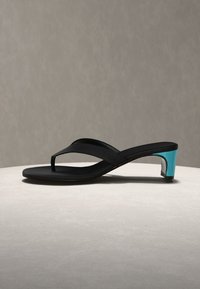Melna thong stila sandaļa ar zemu, spīdīgu tirkīza bloku papēdi uz gaišas virsmas neitrālā fona.