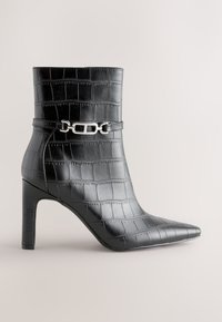 Black croc-patterned leather ankle boot with pointed toe, high heel, and silver metal decorative buckle strap around the ankle.