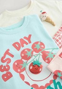 Två bomulls T-shirts: en ljusblå med röd text och tomatgrafik; en krämfärgad med broderad glasskonedetalj.