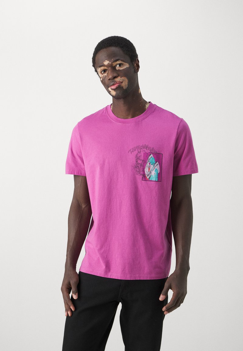 T-shirt à manches courtes en coton rose vif avec un design de poche graphique présentant un imprimé abstrait coloré. Coupe décontractée, col rond.