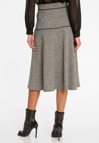 Grauer strukturierten, ausgestellten Rock mit hoher Taille, der mit einem schwarzen Paspelierungsdetail versehen ist. Kombination mit schwarzen Ankle Boots mit offenen Zehen.