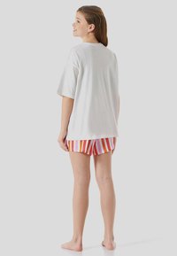 White cotton T-shirt with short sleeves paired with multicolored striped shorts in pink, orange, and red. Simple design without patterns.