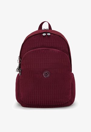Sac à dos bourgogne avec texture matelassée, poignée supérieure et poche zippée. Présente un patch logo et de petits accents matériels.
