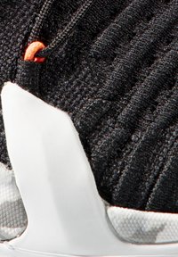 Schwarzer Sportschuh mit einer strukturierten Oberseite, einer auffälligen weißen Sohle und einem orangefarbenen Akzent im Schnürsystem.