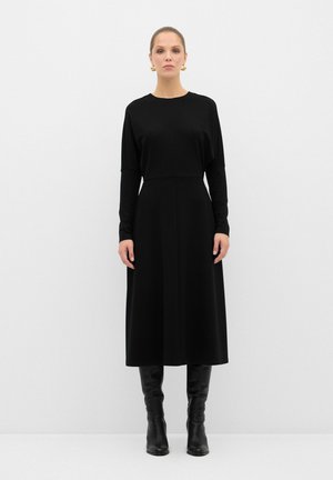 Vestido negro de manga larga con parte superior ajustada y falda en A, hecho de una tela suave. Combinado con botas de cuero negro hasta la rodilla.