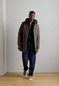 Gray hooded jacket, dark layered hoodie underneath, blue denim pants, beige sneakers. Smooth textures with contrasting colors, standing on wooden floor.