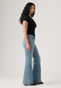 Čierne rebrované body v kombinácii so svetlomodrými rozšírenými džínsami s vysokým pásom a jemným tieňovaním, doplnené čiernymi členkovými topánkami.