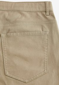 Poche arrière sur pantalon en coton beige avec passants de ceinture visibles et coutures doubles sur tissu uni.