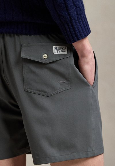 Pilkos, pagamintos iš lygaus audinio, šortai turi užpakalinę kišenę su atvartėliu ir sagos užsegimu, šalia kurios yra prisiūta prekės ženklo etikėtė.