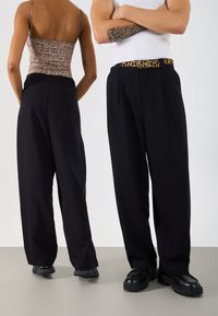 Μαύρο παντελόνι με φαρδιά πόδια που απεικονίζεται από μπροστά και από πίσω. Λείο ύφασμα, ψηλή μέση, σε συνδυασμό με ζώνη με λεοπάρ σχέδιο και χοντρές μαύρες γόβες.