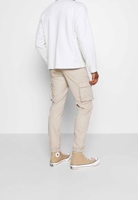 Bílá dlouhá košile s rukávy, béžové cargo kalhoty s kapsami a hnědé vysoké tenisky s bílou podrážkou a hvězdovým logem. Neformální outfit ze zadní strany.