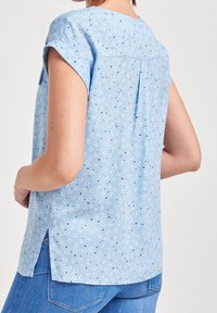 Blusa azzurro chiaro a maniche corte con motivo floreale, dotata di piega sul retro e spacchi laterali, realizzata in un tessuto morbido e leggero.