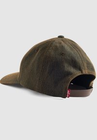 Gorra de mezclilla marrón con visera curvada, costuras oscuras y una correa ajustable marrón en la parte posterior. Presenta una pequeña etiqueta de logo rojo en el lateral.