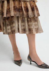 Zapatos de tacón alto con punta afilada, que presentan un acabado metálico texturizado en gris oscuro con acentos metálicos y un delicado detalle de cordones.