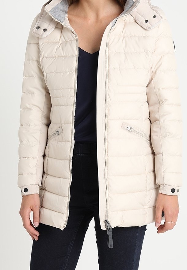 Lys cremefarvet quiltet pufferjakke med lynlås, to sidelommer og en hætte med grå foring. Har en glat, let blank finish.