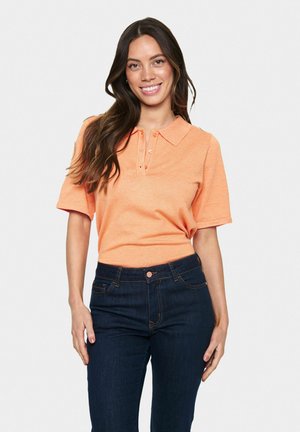 Kortärmad polo i klar orange, med krage och treknappsknäppning. Tillsammans med mörkblå denimjeans.