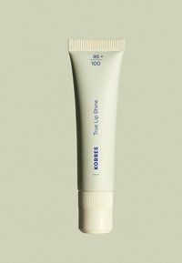 Korres True Lip Shine dans un tube vert clair avec un capuchon à vis blanc. Présente un texte bleu et des détails numériques pour l'identification du produit.