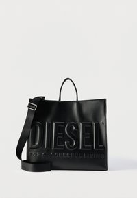 Μαύρη δερμάτινη τσάντα tote Diesel με μεγάλο ανάγλυφο λογότυπο και ρυθμιζόμενο ιμάντα ώμου σε απλό λευκό φόντο.