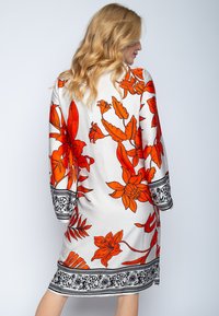Biała sukienka z dużym pomarańczowym wzorem kwiatowym, z czarnymi dekoracyjnymi akcentami wzdłuż rękawów i dolnej krawędzi. Luźny krój.