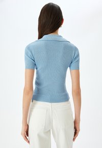 Ljusblå ribbad kortärmad polo med krage, figurnära design, strukturerad yta, och matchad med vita högmidjade byxor.
