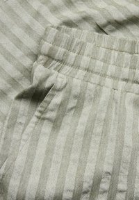 Ljus khaki tyg med vertikala ränder. Elastisk midja, sidofickor och en texturerad finish. Diskret mönsterdetalj som ger visuell intresse.