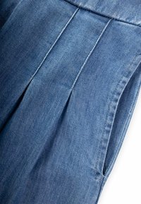 Tumesinise värvusega teksariidest rõivas, millel on nähtavad voldid ja küljetaskud. Materjal on sileda tekstuuriga, millel on peened toonivarjundid.