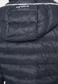Navy Puffer-Jacke mit horizontalem Steppmuster, abnehmbarer Kapuze und weißem Logo auf dem Rücken. Glatte, glänzende Textur.
