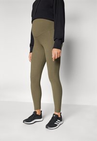 Μαμά  leggings σε ελαιόδιο ύφασμα, εφαρμοστό σιλουέτα, ψηλή μέση, συνδυασμένα με μαύρα αθλητικά παπούτσια και μπλούζα με μακριά μανίκια.