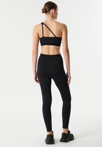 Černý sportovní crop top s jedním ramínkem a odpovídajícími legínami s vysokým pasem. Hladká textura, minimalistický design a žádné viditelné vzory.
