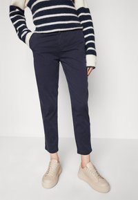 Marina chinos med slim fit, tillsammans med ljusbeige sneakers. Tröjan är randig i marinblått och vitt och har en lös stickning.