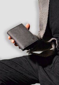 Black leather wallet with a sleek design, rectangular shape, smooth texture, and a subtle logo on the front. Accented by a patterned fabric background.