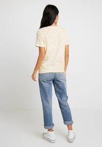 Camiseta amarilla a rayas con un ajuste relajado, mangas cortas y cuello redondo, combinada con jeans azul claro y zapatillas blancas.