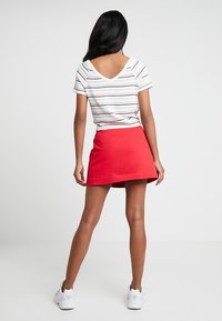 Pasiasty, krótki top z dekoltem w kształcie litery V; połączony z jasnoczerwoną spódnicą A-line; model nosi białe trampki.