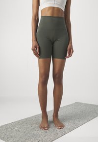 Olive zielone, wysokowodne szorty rowerowe wykonane z elastycznej tkaniny, charakteryzujące się gładką fakturą i dopasowanym krojem, zestawione z białym crop topem.